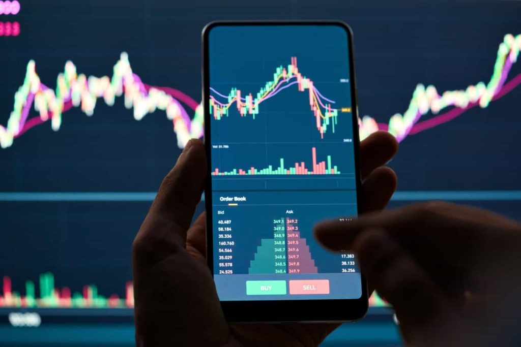 Crypto trader investor broker holding finger using cell phone app executing financial stock trade market trading order to buy or sell cryptocurrency shares thinking of investment risks profit concept.