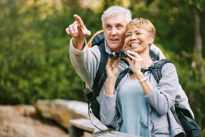 Elderly, couple hiking and bird watching with adventure outdoor, hike together and fitness for active lifestyle. Nature, trekking and senior man pointing and woman with binocular, freedom and travel