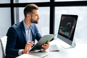 Thoughtful focused successful caucasian male stock investor, broker, financial adviser, sits at work desk, looks at computer, pensively analyze risks and prospects, rise or fall of cryptocurrency coin