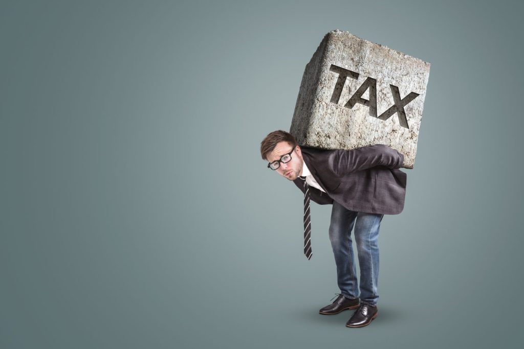 Businessman bending under a heavy stone with the word TAX printed on it