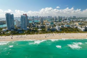 Travel destination in United States. South Beach sandy surface with tourists relaxing on hot Florida sun. Tourism infrastructure in southern USA. Miami Beach city with high luxury hotels and condos