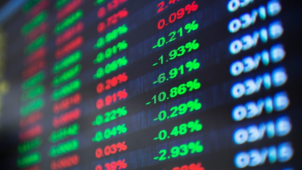 A blurry, close-up shot of a digital stock market display screen with glowing numbers and percentages in green and red against a dark background. Clearly visible green percentages include -0.21%, -1.93%, -6.91%, -10.86%, -0.29%, -0.48%, and -2.93%. Prominent red percentages include 2.4%, 0.09%, 0.26%, 0.01%, 0.22%, 0.04%, 0.03%, and 0.39%. A column of light blue text, mostly appearing as '03/18', repeats down the right side of the screen.