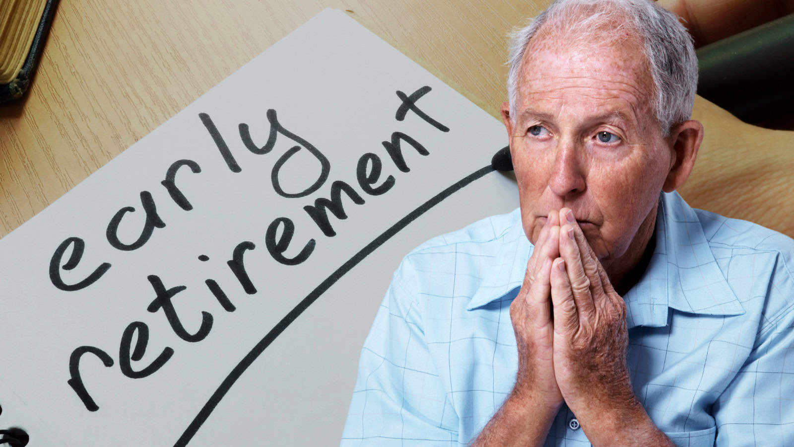A pensive older man with gray hair, wearing a light blue plaid shirt, holds his clasped hands under his chin while looking thoughtfully to the left. Partially visible on the left is a white notepad with the words 'early retirement' written in black script and underlined. A wooden desk surface and the edge of a book are in the background.