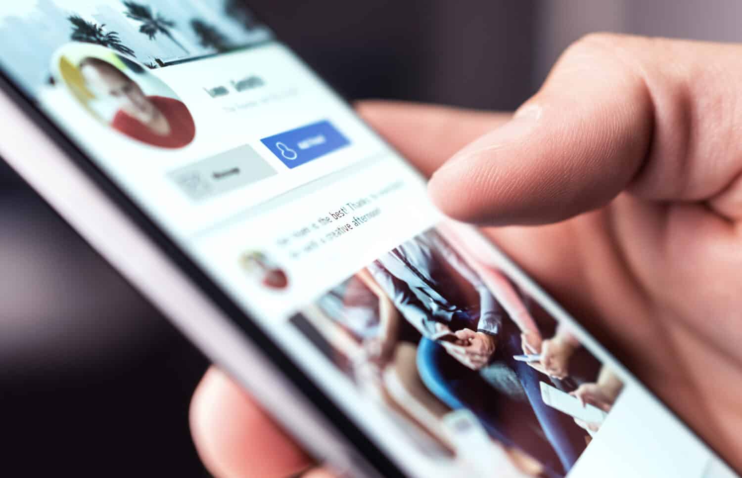 A person reads updates on a social media profile using a smartphone.
