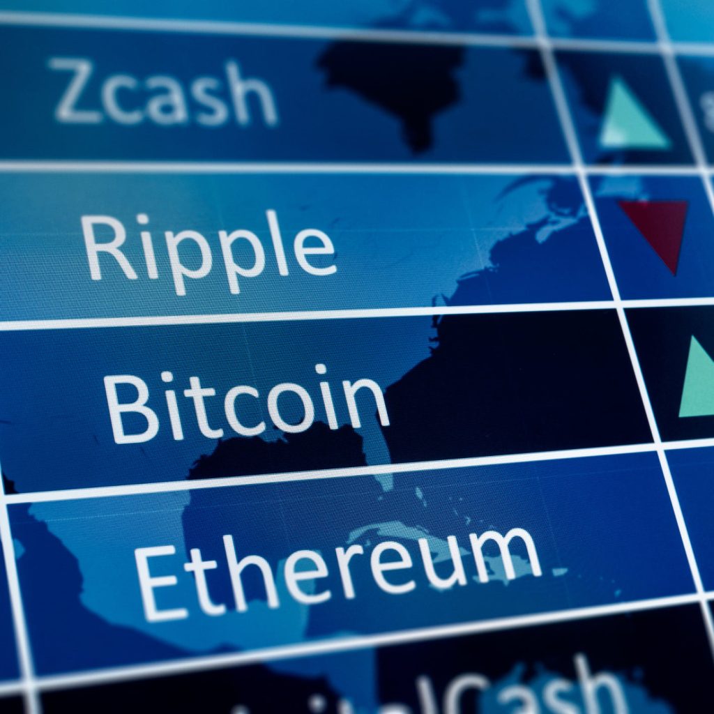 A close-up photograph of a blue digital screen showing a list of cryptocurrency names: Zcash, Ripple, Bitcoin, and Ethereum, in white text. A faint world map overlay and white grid lines are visible in the background. To the right of the names, green upward-pointing and red downward-pointing triangular arrows indicate market trends.