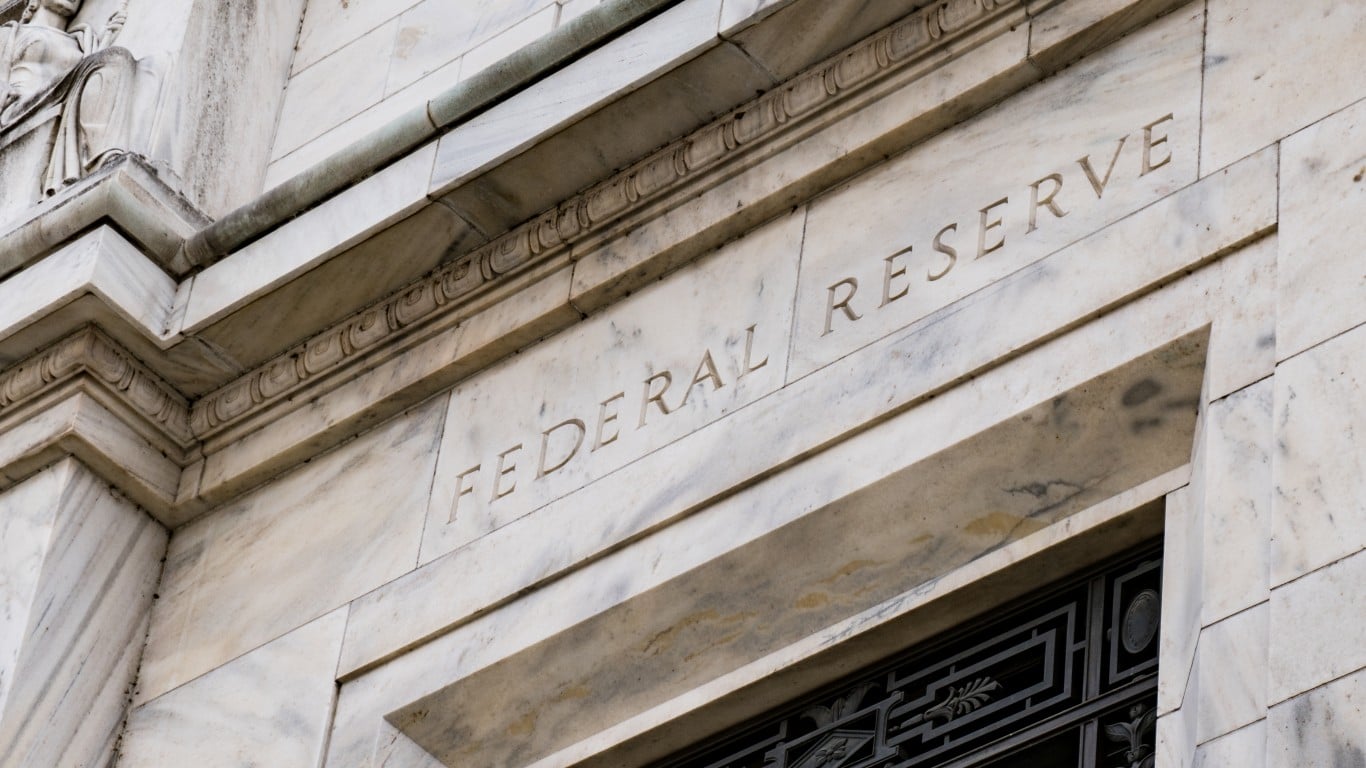 A close-up, low-angle view of the white marble exterior of the Federal Reserve building. The words 'FEDERAL RESERVE' are carved in capital letters into the stone facade, which exhibits subtle veins and a weathered appearance, with architectural cornices and molding details visible above the inscription.