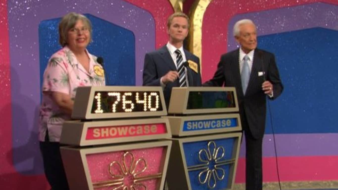 Three people stand on a colorful television game show set. On the left, an older woman with short gray hair and glasses smiles, wearing a pink floral blouse. In the center, a man with short blonde hair in a dark suit and striped tie looks forward seriously. On the right, an older man with white hair in a dark suit and light blue tie holds a microphone. In front of the woman and the center man are two podiums with digital displays. The left display shows the numbers '17640' in white, with the word 'SHOWCASE' in red below it. The right display also shows 'SHOWCASE' in blue.