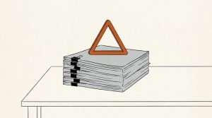 Illustration: an orange warning triangle standing on top of a thick clipped stack of paperwork on a desk