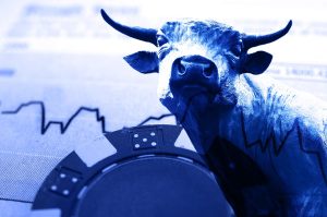 A monochromatic blue-toned image shows a statue of a bull, positioned centrally and looking forward. In the background and overlaid on the bull's body is a black line graph depicting market fluctuations. In the foreground, partially visible on the bottom left, is a dark blue casino chip with white markings.