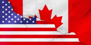 A distressed composite image featuring the flags of the United States and Canada. On the left, the blue field with white stars and red and white stripes of the US flag is visible. On the right, the red maple leaf and red bands of the Canadian flag appear on a white background. Both flags are depicted with a textured, cracked, and worn appearance, suggesting tension or strain in their relationship.