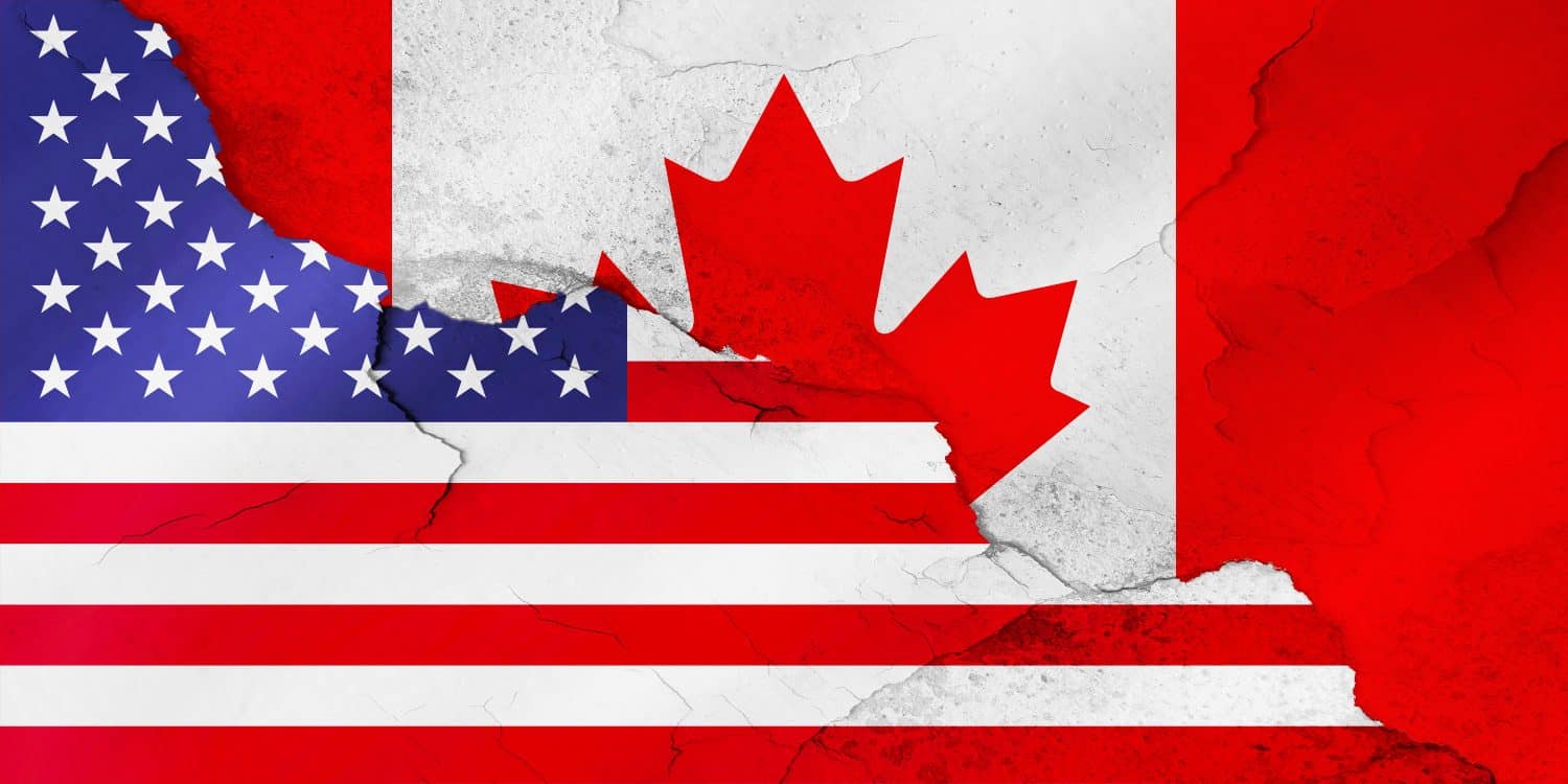 A distressed composite image featuring the flags of the United States and Canada. On the left, the blue field with white stars and red and white stripes of the US flag is visible. On the right, the red maple leaf and red bands of the Canadian flag appear on a white background. Both flags are depicted with a textured, cracked, and worn appearance, suggesting tension or strain in their relationship.