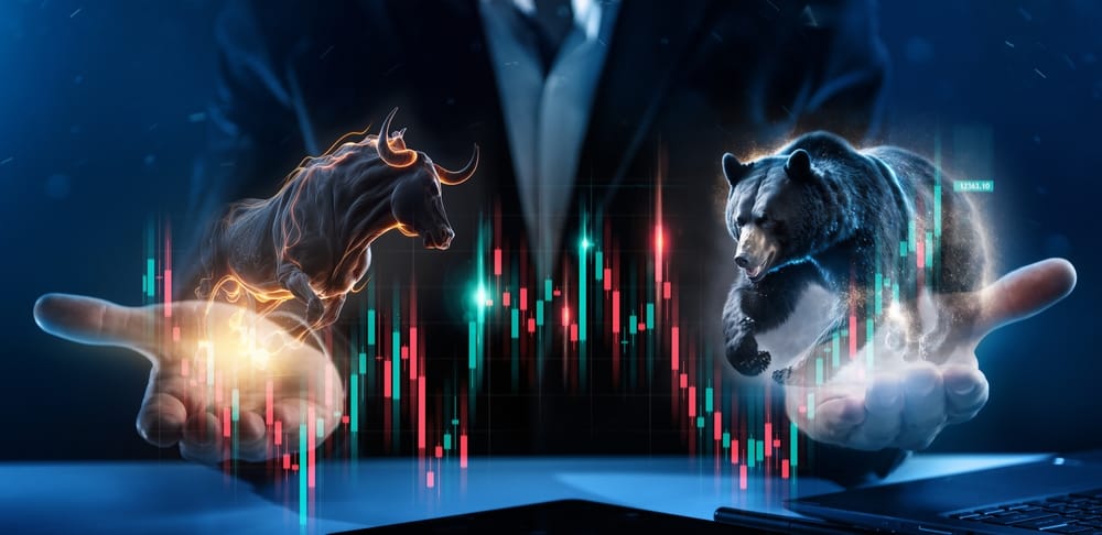 A stylized digital image shows two human hands emerging from a dark background, each holding a glowing animal. The left hand holds a powerful, golden-outlined bull, poised to charge upward. The right hand cradles a strong, blue-outlined bear, seemingly pushing downward. Between and around the hands are numerous vertical candlestick charts in vibrant red and teal, representing market data. A faint figure in a suit is visible in the background. The overall tone is dramatic and focused on financial market concepts.