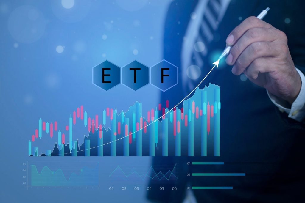 A close-up of a person's hand holding a pen, pointing towards a glowing white arrow that curves upwards from a digital financial chart. The background is a gradient of deep to light blue, with multiple overlapping transparent graphs, including candlestick and bar charts in red, blue, and white. Three hexagonal shapes at the top center display the letters 'E', 'T', and 'F' in bold white text. The overall scene conveys market analysis, growth, and strategic investment.