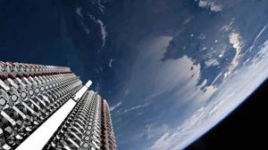 A wide-angle view from space shows countless white and metallic satellites arranged in long, stacked columns, appearing to launch or deploy against the backdrop of Earth's curved horizon. The blue atmosphere transitions to the dark void of space, with scattered clouds visible on the planet's surface.